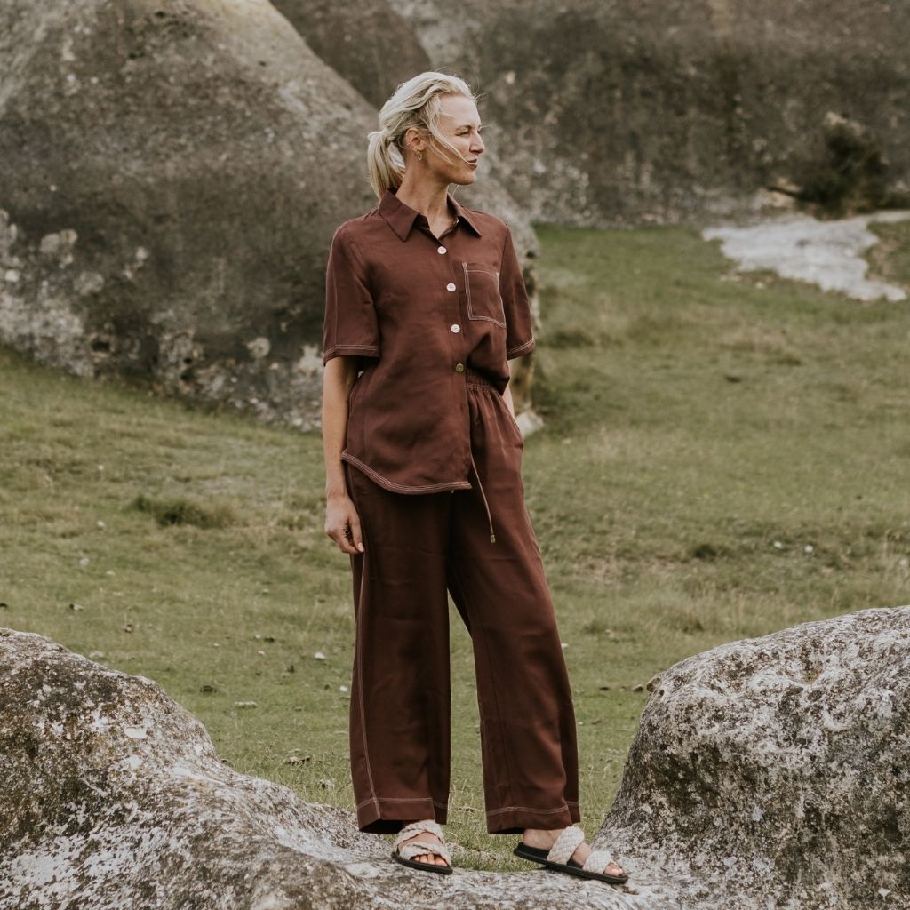 Person wearing a brown outfit standing on a grassy area with large rocks.