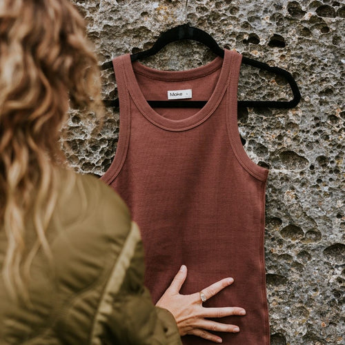 Brown tank top on a hanger against a textured stone wall with a person partially visible.