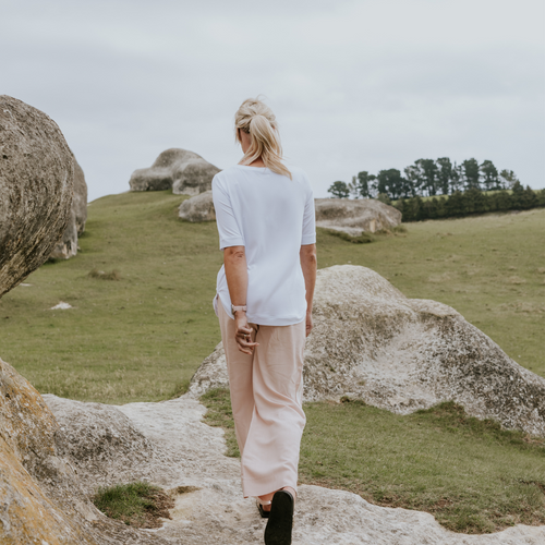 Person standing on a rocky path in a natural landscape with green grass and trees.