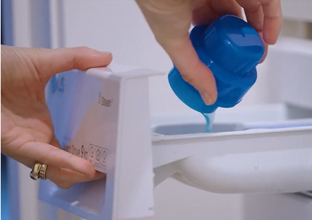 Person pouring a blue liquid from a bottle into a white container with a blue cap.