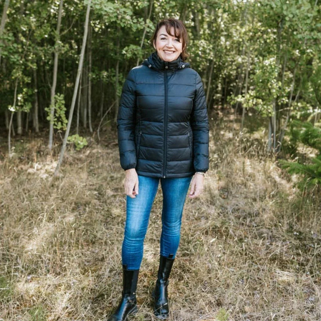 Woman wearing a black puffer jacket and blue jeans standing in a forest.