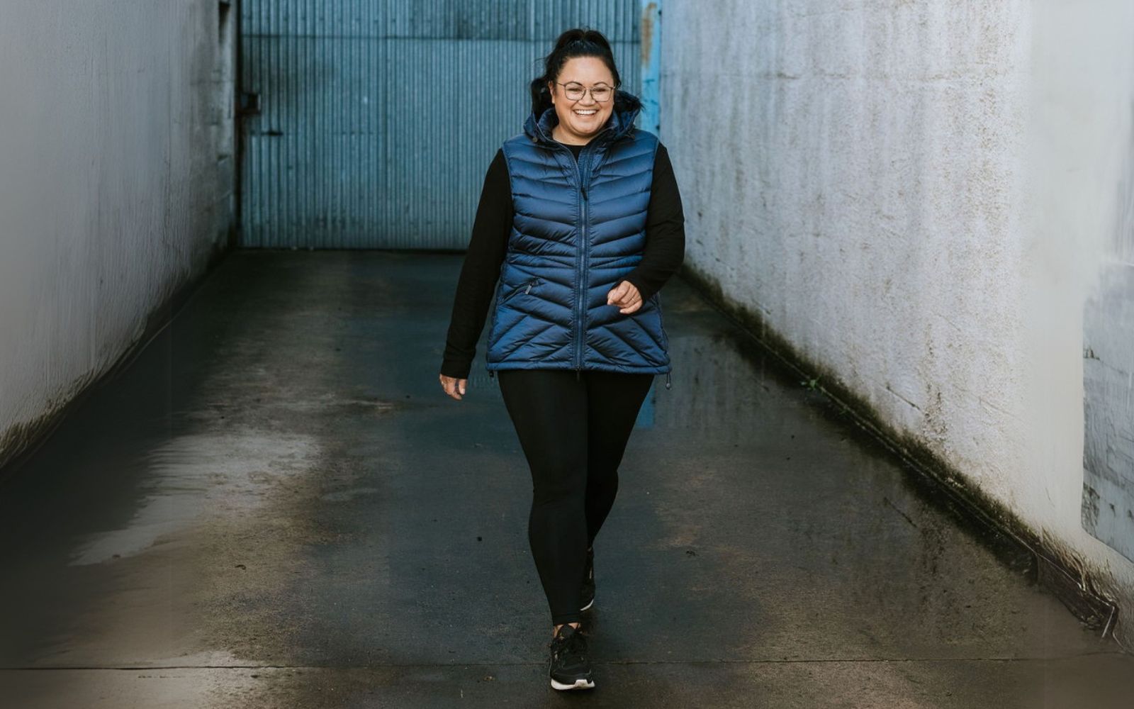 Person wearing a blue puffer vest walking in a narrow alleyway.