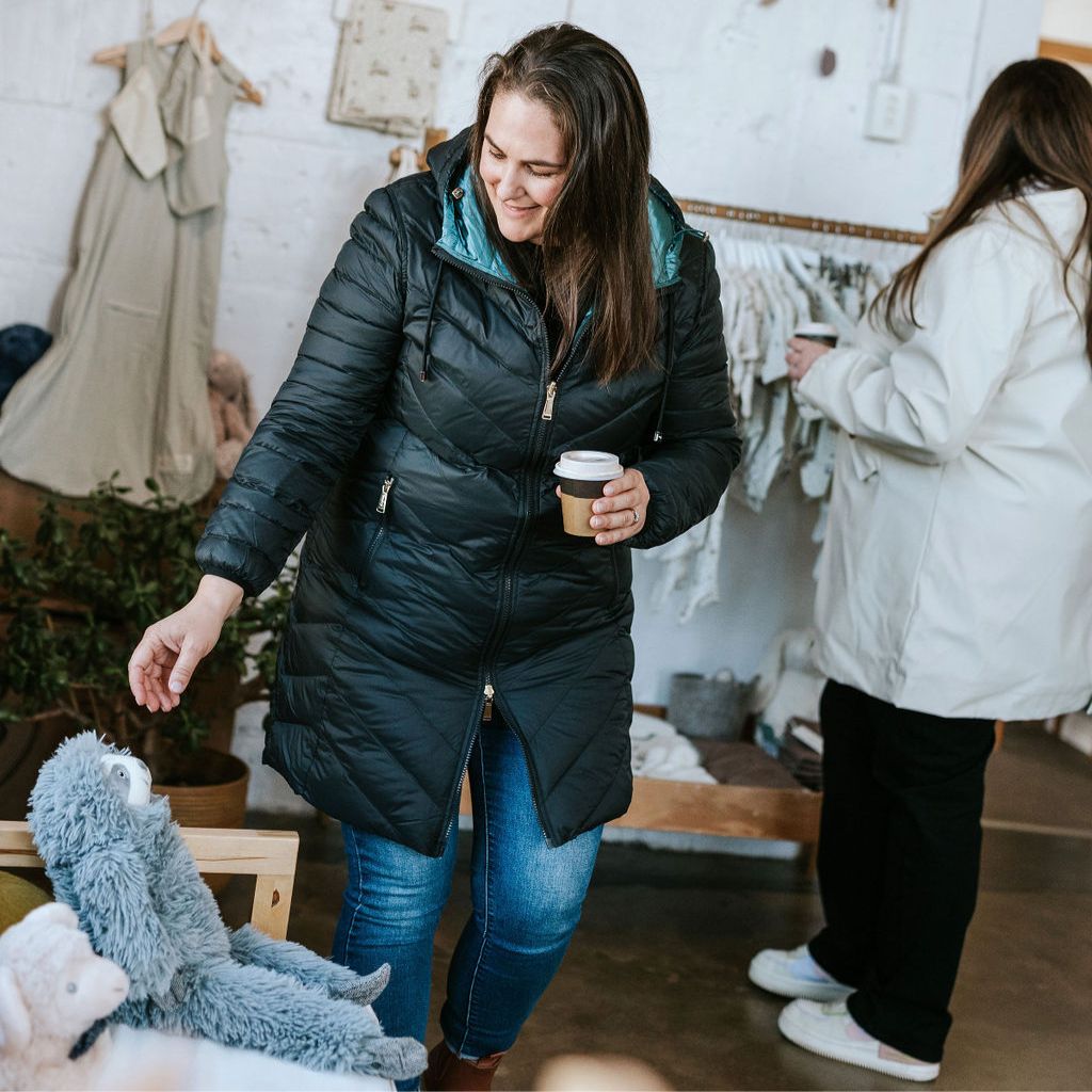A woman's reversible down coat with a quilted design, main color is black with empire blue lining visible at the hood, zipper front, and hood with adjustable drawstrings.