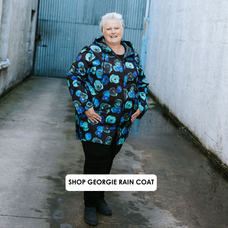 Person wearing a colorful raincoat standing in an alleyway with text 'Shop Georgie Rain Coat'.
