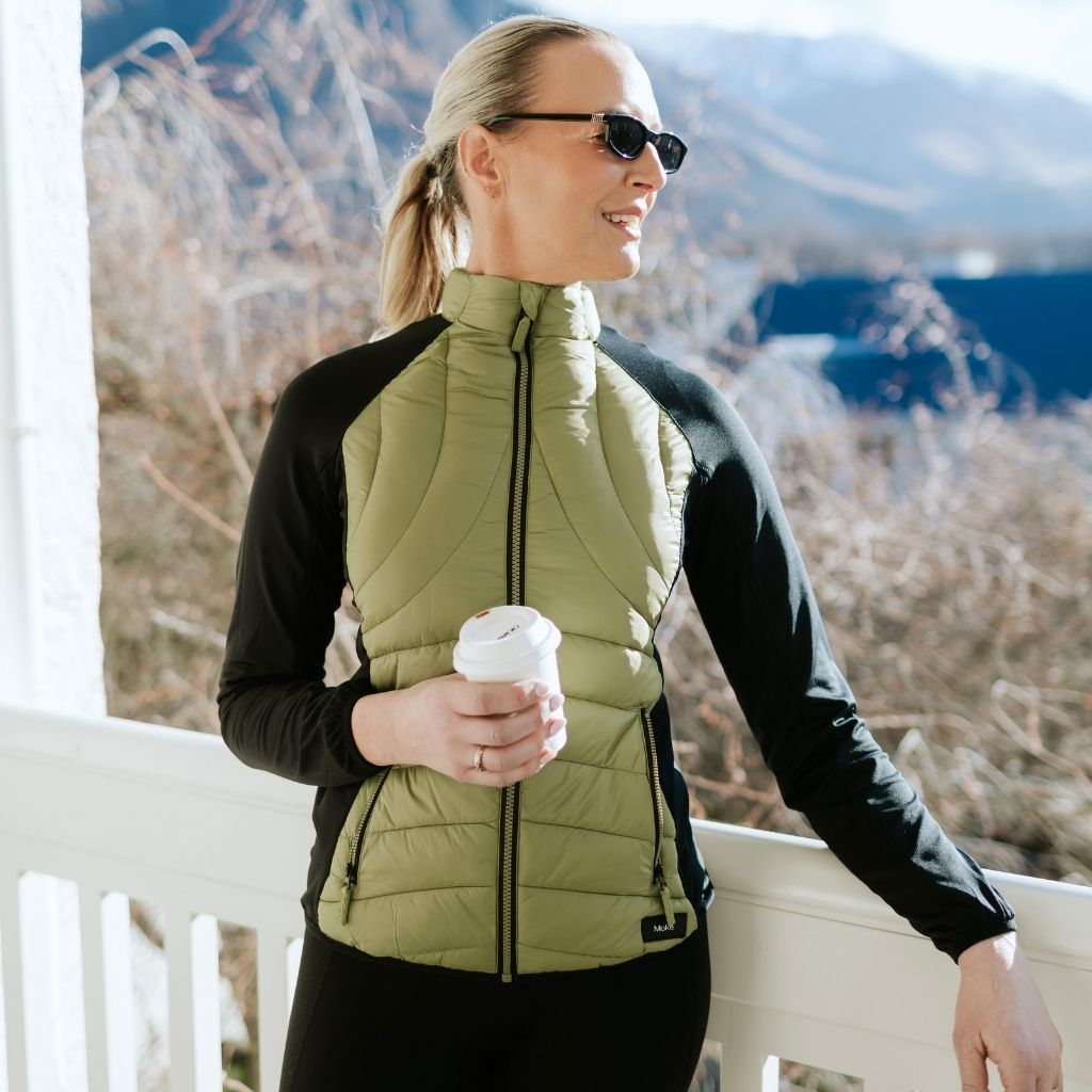 Woman wearing a Moke olive green puffer vest and black long-sleeve top outdoors.