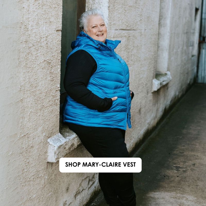 Woman wearing a blue puffer vest leaning against a wall with text 'Shop Mary-Claire Vest'.