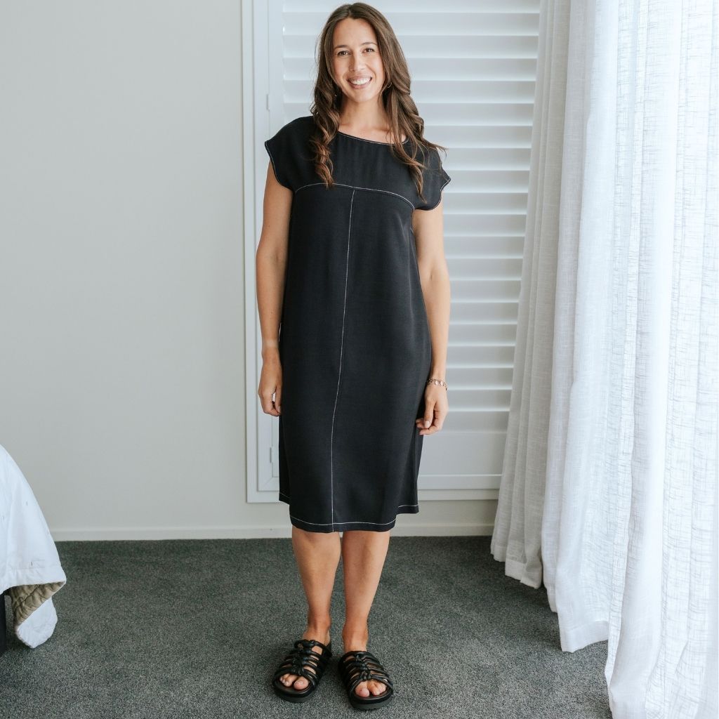 Woman wearing a Moke black knee-length dress with contrast stitching and black sandals.