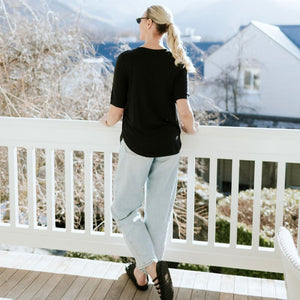 Woman wearing a black Moke t-shirt and light blue jeans standing on a white balcony.