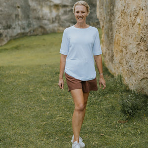 Woman wearing a Moke light blue t-shirt and brown shorts walking outdoors.