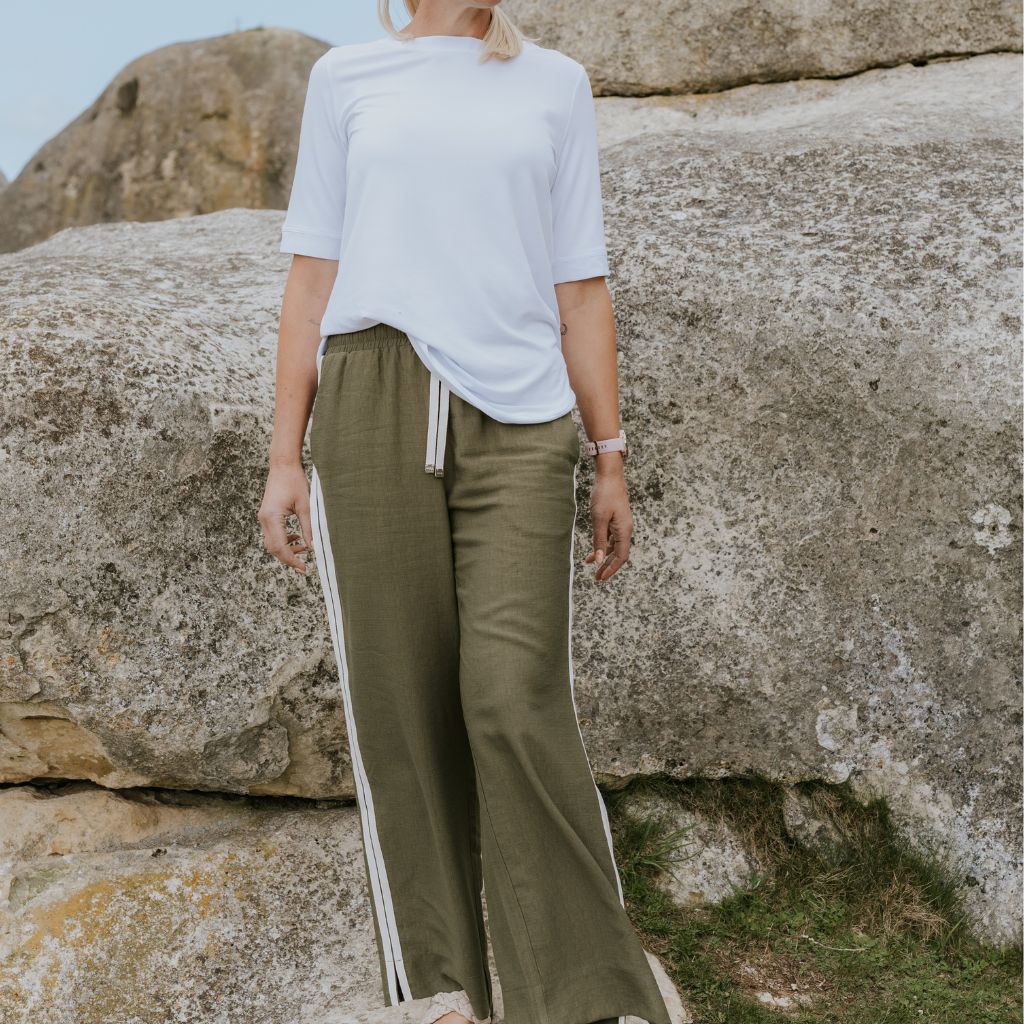 Woman wearing a white t-shirt and Moke olive green wide-leg trousers with side stripes.