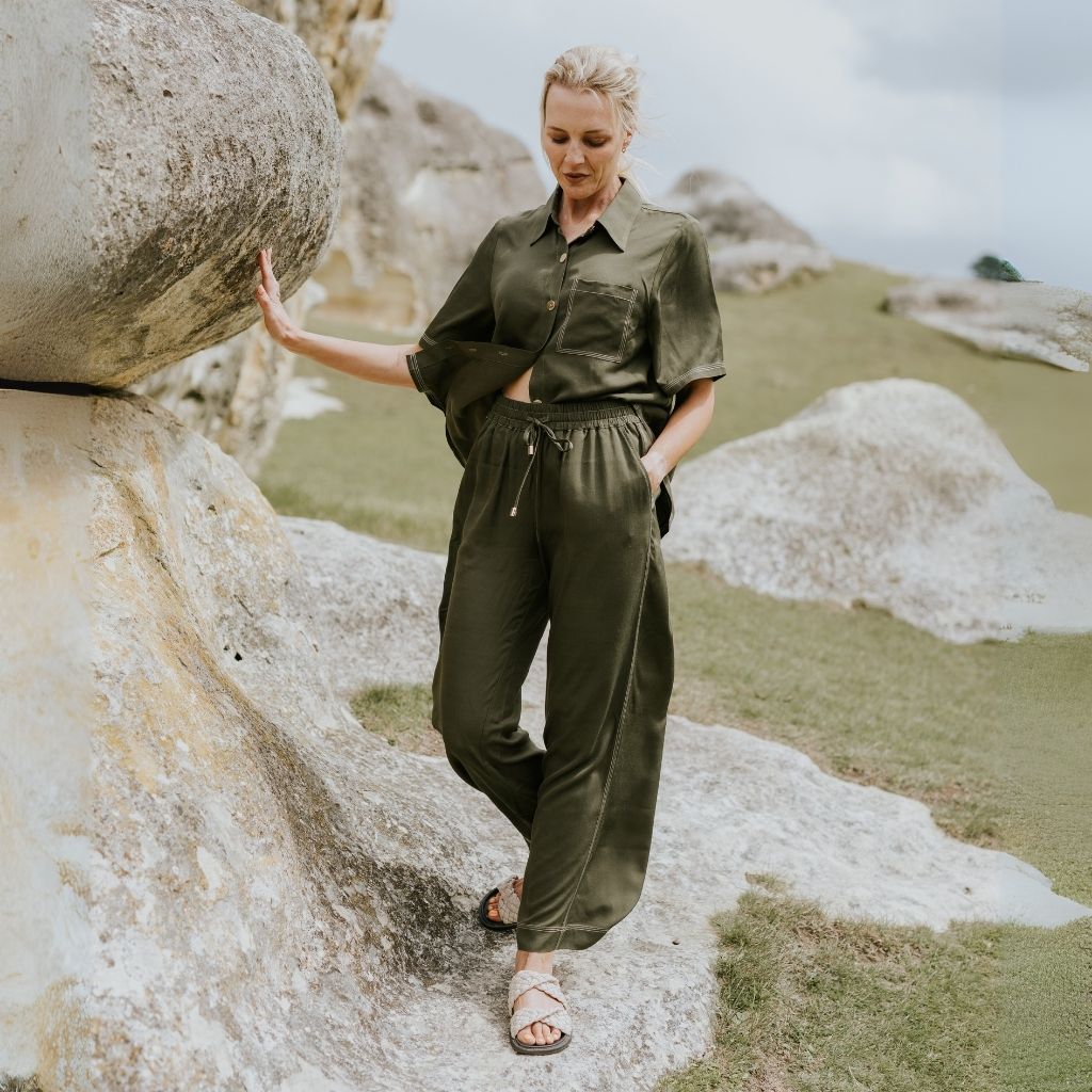 Woman in a green outfit standing near large rocks in a natural landscape